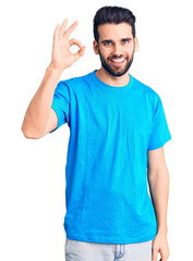 Fototapeta premium Young handsome man with beard wearing casual t-shirt smiling positive doing ok sign with hand and fingers. successful expression.