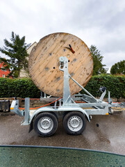 Giant wooden reel of optic fiber cable on a trailer at an installation site, with urban...