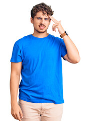 Fototapeta premium Young handsome man with curly hair wearing casual clothes shooting and killing oneself pointing hand and fingers to head like gun, suicide gesture.