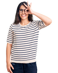 Brunette teenager girl wearing casual clothes and glasses doing ok gesture with hand smiling, eye looking through fingers with happy face.