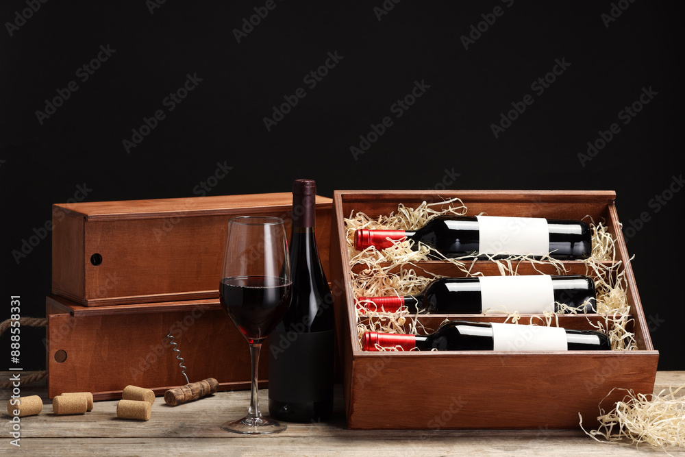 Poster Box with wine bottles, glass, corks and corkscrew on wooden table against black background