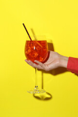 Woman with glass of refreshing cocktail on yellow background, closeup