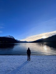 silhouette of a person by a lake and mountains