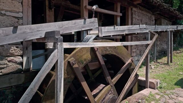 Water cascading from rustic wooden flume chute turns large wooden mill waterwheel