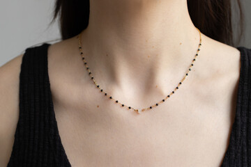 Simple beaded necklace on female neck. Model posing with jewelry in black top. Elegant pendant on young woman chest