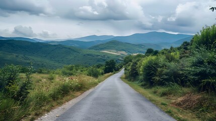 Fototapeta premium Countryside asphalt road surrounded by green foliage and rolling mountains