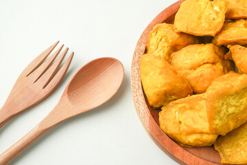 Flat Lay Photo of Fried yellow tofu served on wooden plate next to wooden spoon and fork. Tahu Takwa is a specialty food from Kediri, East Java, Indonesia. Concept for Plant based protein.