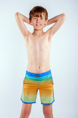 Obraz premium Smiling young teen beach boy in colorful swim trunks, standing with his hands behind his head 