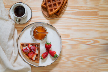 freshly made breakfast on a beautiful morning with honey, strawberries, and waffles
