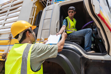 Asian dedicated truck driver examining shipment papers next to a freight truck, ensuring accuracy...