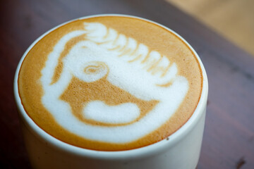 Hot cafe latte in a white cup, with unique latte art foam. Served on wooden table, in a cozy cafe environment