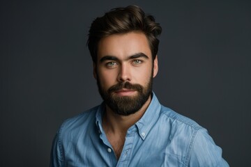 Portrait of confident European businessman with beard and dark hair in blue shirt looking at camera Shot in studio on dark gray background