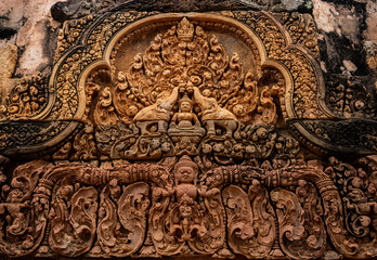 Pediment containing bas relief carved in red sandstone of ancient figures at Banteay Srei -citadel of women and beauty- Hindu temple dedicated to god Shiva and Parvati, Siem Reap, Cambodia