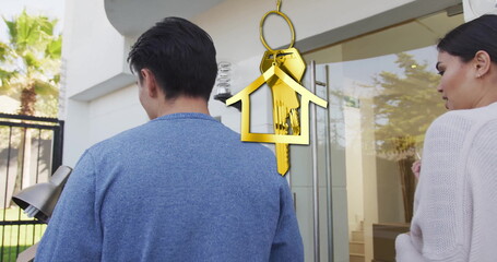 Image of gold house key and key fob over happy diverse couple moving in to new home
