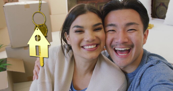 Image of gold house key and key fob over happy diverse couple at new home