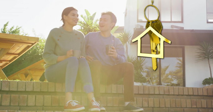 Image of gold house key and key fob over diverse couple drinking tea at new home