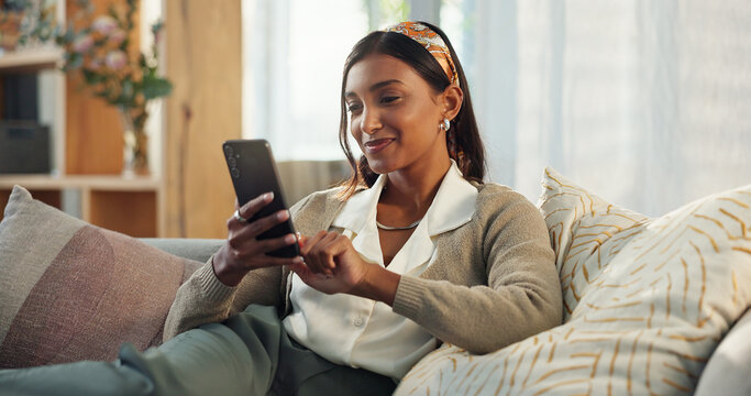 Cellphone, indian woman and smile on sofa in home in living room, texting and communication on mobile. Lounge, couch and happy person for online dating app, notification and internet relationship