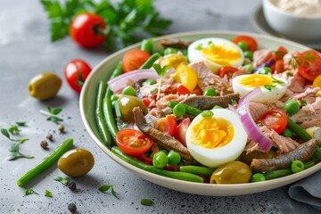 Salad with tuna anchovies eggs vegetables olives tomatoes and onions on gray background
