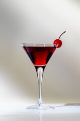 Black Manhattan cocktail with whiskey and red vermouth garnished with maraschino cocktail cherry in martini glass. Beige background, hard light
