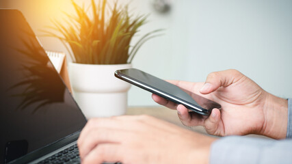 Laptop and phone for online shopping, internet searching. Trader man holding smartphone and typing on laptop keyboard. Communication and trade concept. Close up.