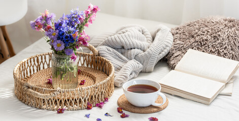 Cup of tea, a bouquet of wildflowers, book and knitted element.