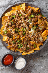 Cheesy Beef Nachos Tortilla chips covered with seasoned ground beef and melted cheese closeup on the plate on the table. Vertical top view from above