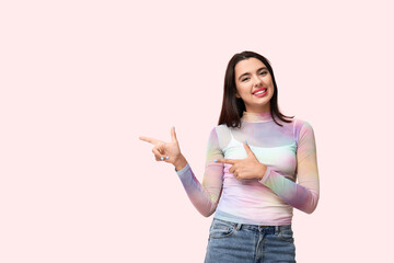 Beautiful young happy woman pointing at something on pink background