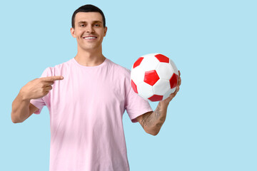 Handsome young man pointing at soccer ball on blue background