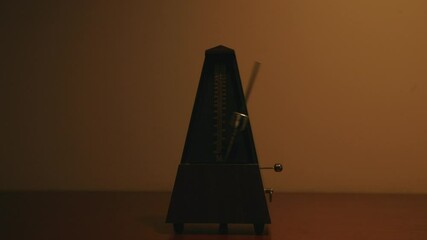 Metronome that is moving back and forth that is it above by a light that is following the swinging pendulum.