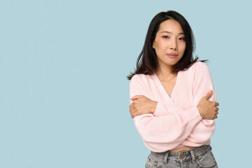 Obraz premium Young Asian woman hugging herself on blue background
