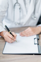 Fototapeta premium Close-up of a medical professional writing on a clipboard, wearing a white coat with a stethoscope, in a clinical environment.