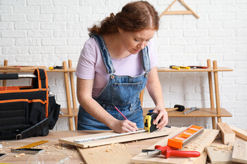 Female carpenter measuring plank length with tape in workshop