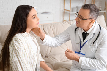 Obraz premium Mature doctor examining neck of ill young woman at home