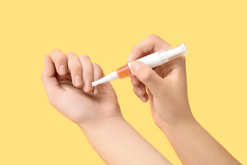 Female hands with cuticle oil stick on yellow background