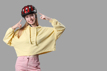 Beautiful young woman pointing at helmet on grey background