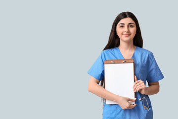 Obraz premium Beautiful young female doctor with clipboard and stethoscope on white background