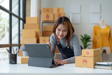 Startup small business entrepreneur SME freelancer. Young woman checks stock on clipboard and parcels at home office. Boxes. Laptop. Online. Marketing. Packaging. Shipping. SME. Ecommerce concept.