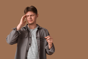 Young man with headache pressing fingers to temple on brown background