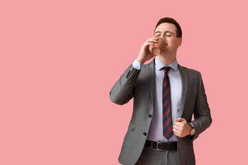 Handsome young man drinking fresh coffee on pink background