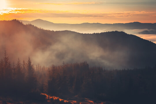 A beautiful sunrise over a misty mountain range. The sun is shining brightly, casting a warm glow on the landscape. The fog is slowly dissipating, revealing the peaks of the mountains in the distance.