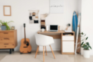 Blurred view of teenager's room with workplace, organizers and surfboard