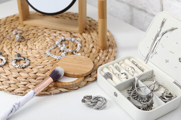 Box with different stylish jewelry, powder and makeup brush on table, closeup