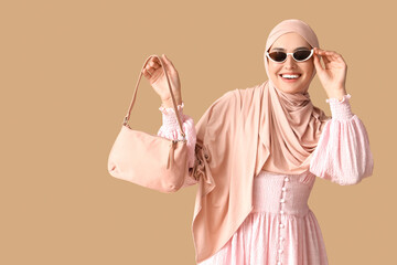 Stylish Muslim woman with bag on beige background