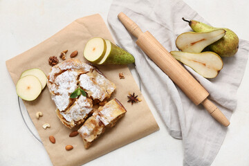 Pieces of tasty pear strudel with fresh fruits and rolling pin on beige background