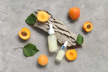 Bottles of cosmetic oil with fresh apricots and tree bark on grey background