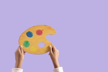 Child with paint palette on lilac background