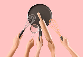 Female hands with different baking utensils on pink background