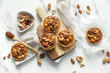 Fototapeta premium Tasty tarts with different nuts and caramel on wooden board against grunge white background