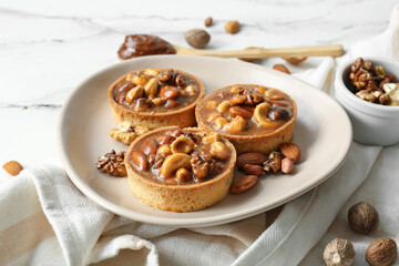 Tasty tarts with nuts and caramel on plate against grunge white background