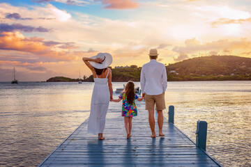 A family walks down a pier in the Caribbean sea during beautiful sunset time at their holiday...